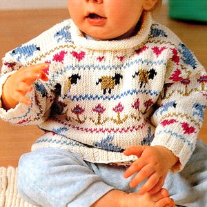 Puede incluir: Un jersey de punto blanco para bebé con un patrón colorido de ovejas, flores y anclas. El jersey tiene cuello alto y mangas largas.