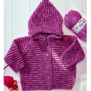 May include: A pink knitted baby cardigan with a hood and button closure. The cardigan is made with a textured stitch and has a subtle ombre effect. The yarn is labeled "Wendy Petite Pan."