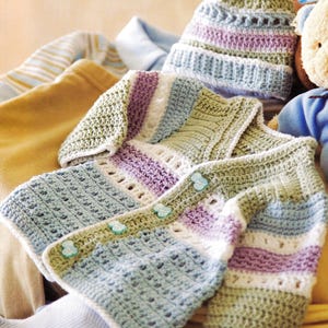 Może przedstawiać: Ręcznie robiony zestaw dla dziecka na szydełku, składający się z kardiganu i pasującej czapki. Zestaw jest w pastelowych kolorach niebieskim, zielonym, fioletowym i białym. Kardigan ma trzy jasnoniebieskie guziki w kształcie kwiatów. Czapka ma wzór w paski.