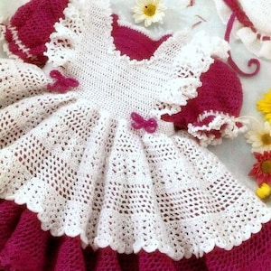May include: A white crocheted baby dress with a pink satin bow and a pink knitted bodice.