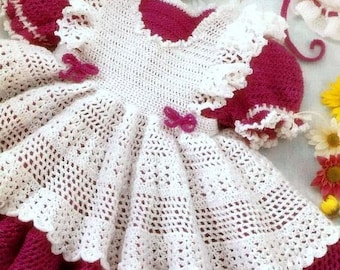 May include: A white crocheted baby dress with a pink satin bow and a pink knitted bodice.