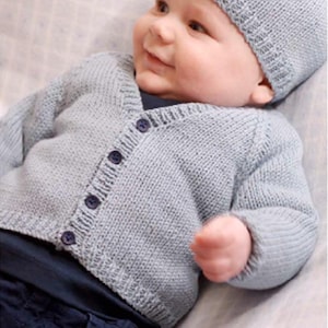 May include: A light blue knitted cardigan with a V-neck and button closure. The cardigan is worn by a baby wearing a light blue knitted hat.
