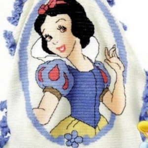 May include: A crocheted blanket featuring a cartoon image of Snow White in a blue dress and yellow skirt. The blanket is white with a blue border and a red bow on Snow White's head.