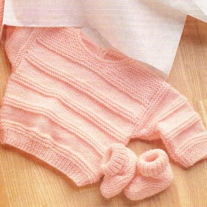May include: A pink knitted baby sweater and matching booties. The sweater has a ribbed pattern and the booties have a simple knit design.