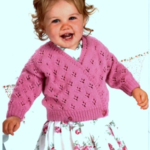 May include: A pink knitted cardigan with a V-neck and a button closure. The cardigan has a delicate lace pattern.