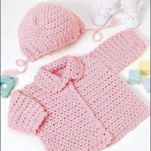 Può includere: Un cardigan rosa per neonato lavorato a uncinetto con un cappello abbinato. Il cardigan ha un colletto e maniche corte. Il cappello ha un laccio.
