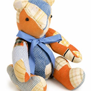 May include: A stuffed teddy bear constructed from various fabric patches in shades of orange, blue, and cream. The bear features a patchwork design with plaid, gingham, and striped patterns, black bead eyes, and a blue ribbon tied around its neck.