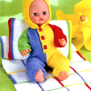 May include: A doll wearing a knitted, multi-colored jumpsuit with a hood. The jumpsuit is yellow, blue, green, and red. The doll is sitting on a white and blue knitted blanket with a matching pillow. A yellow pinwheel is in the background.