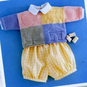 May include: A knitted baby sweater with a patchwork design featuring different coloured squares with embroidered shapes. The sweater has a white collar and is paired with yellow and white checked shorts.
