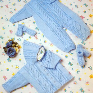May include: A set of baby clothes in a light blue color, including a hooded sweater, a knitted jumpsuit, and a pair of booties. The clothes are made with a cable knit pattern.