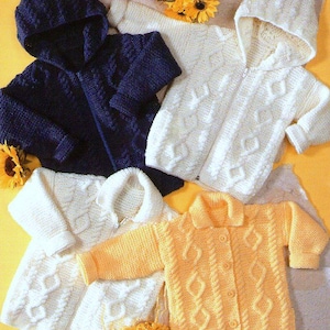 May include: Four knitted baby sweaters in different colors: navy blue, white, and yellow. The sweaters have a cable knit pattern and are all hooded.