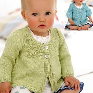 May include: A light green knitted cardigan with a flower detail on the front and a single button closure. The cardigan is worn by a baby.