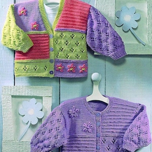 May include: Two knitted cardigans for babies, one in green, pink, and purple with a button fastening and the other in purple with a button fastening.