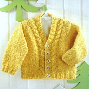Puede incluir: Un cárdigan de punto amarillo con un patrón de trenza y cierre de botones.
