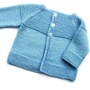May include: A light blue knitted baby cardigan with a button closure. The cardigan has a simple design with a ribbed collar and cuffs.