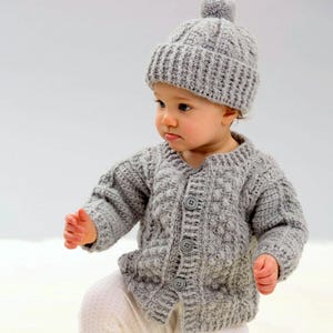 May include: A gray crocheted cardigan with buttons and a matching gray crocheted hat with a pom-pom on top.