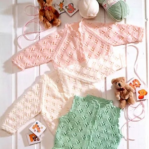 May include: Three knitted baby garments in pink, white, and green. The garments are a cardigan, a long-sleeved sweater, and a sleeveless vest. Each garment features a delicate lace pattern.