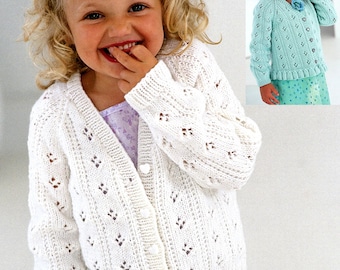 May include: A white crocheted cardigan with a button-up front and a delicate openwork pattern. The cardigan is worn by a young girl with blonde curly hair.