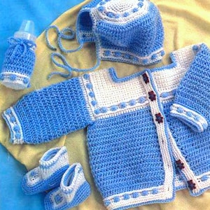 Puede incluir: Un conjunto de ropa de bebé de punto azul con ribetes blancos y botones, un gorro a juego y botines.