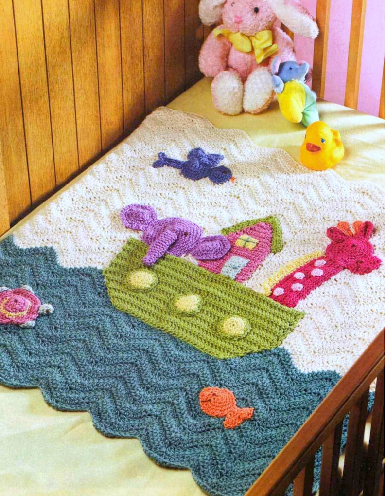 May include: A crocheted baby blanket with a blue, green, and white chevron pattern. The blanket features a crocheted ark with a pink giraffe, purple elephant, and a small pink house. There are also crocheted fish, a turtle, and a bird on the blanket.