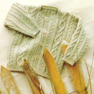 May include: A pale green cable-knit cardigan. The round-neck sweater has a button-up front and a textured design. The buttons are a light beige colour. The garment is likely made of wool or a similar soft material.