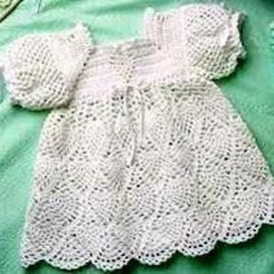 May include: White crocheted baby dress with a scalloped hem and a tied bow at the neckline.