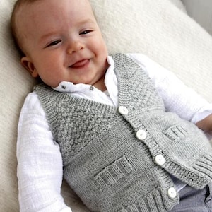 Può includere: Un gilet di maglia grigia con chiusura a bottone e due tasche. Il gilet è indossato da un bambino con una camicia bianca sotto.