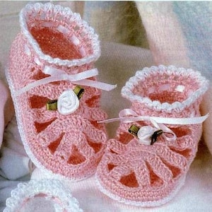 May include: A pair of pink crocheted baby booties with white trim and a white satin ribbon. The booties have a flower embellishment on each.