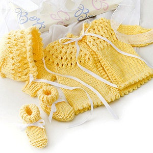 May include: A yellow knitted baby outfit set including a hat, cardigan, and booties. The set is made with a delicate stitch pattern and features a white ribbon.
