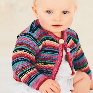 Puede incluir: Un cárdigan de bebé a rayas de colores con ribete rosa y cierre de dos botones. El suéter de punto presenta rayas horizontales en varios colores, incluyendo rojo, azul, amarillo y negro. Un pequeño botón en forma de flor está en el lado izquierdo.