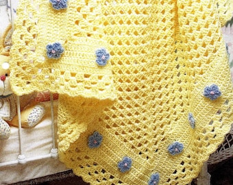 May include: A yellow crocheted baby blanket with blue flower accents. The blanket is folded and draped over a white cot.