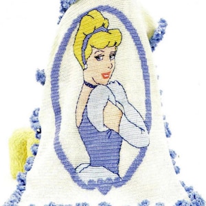 Könnte beinhalten: Eine weiße Häkeldecke mit einem blauen Häkelrand. Die Decke zeigt ein Bild von Aschenputtel in einem blauen Kleid und einem weißen Handschuh. Das Bild ist von einem blauen Oval umgeben.