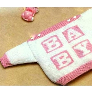 May include: A white knitted baby sweater with pink trim and the word "BABY" spelled out in pink blocks.