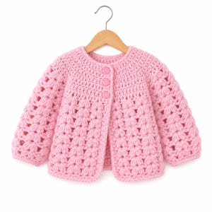 Puede incluir: Una chaqueta de punto de manga larga en color rosa claro con un patrón de ganchillo de punto puff texturizado en todo el cuerpo y las mangas. La prenda tiene cuello redondo, dobladillo recto y se abrocha al frente con tres botones circulares rosas.