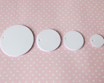 May include: Four white round paper gift tags of different sizes on a pink background with white polka dots.