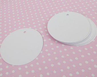 May include: A stack of ten white round paper gift tags with a hole punched in the top. The tags are on a pink background with white polka dots.