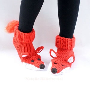 Puede incluir: Un par de pantuflas de zorro de crochet rojo con detalles blancos y ojos negros. Las pantuflas tienen una cola esponjosa.
