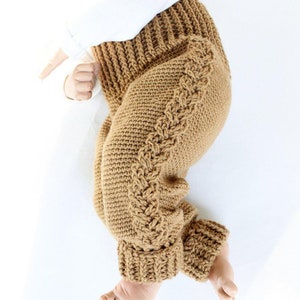 May include: A pair of brown crocheted baby trousers with a braided design on the side.