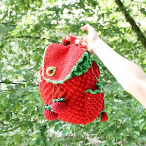 Peut inclure: Un sac à dos rouge en crochet en forme de fraise avec des feuilles vertes et un petit charme de fraise rouge.