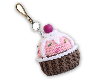 May include: A crocheted cupcake keychain with pink frosting, white icing, and brown sprinkles. The keychain has a brown cord loop.