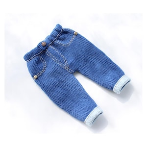 May include: Blue knitted baby pants with a denim look and light blue trim. The pants have a button closure and faux pockets.