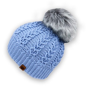 May include: A light blue knitted beanie with a gray faux fur pom pom. The beanie has a cable knit pattern.
