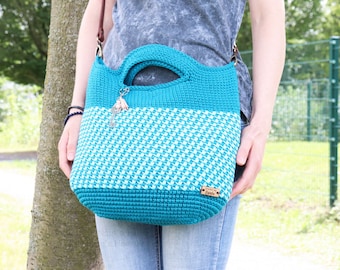 May include: A teal and white crocheted tote bag with a brown leather strap. The bag has a small wooden tag that says "From the Hook".