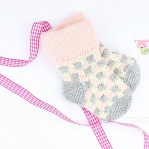 Könnte beinhalten: Ein Paar gestrickte Babysocken in Rosa, Grau und Gelb mit einem rosa-weiß karierten Band. Handgefertigt & Handgestrickt von Natalia Wertel.
