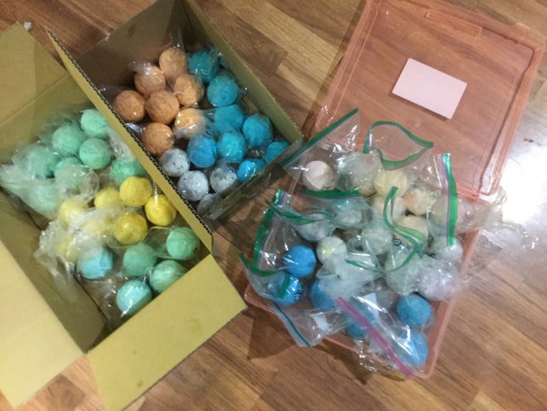 May include: Assortment of colorful, spherical craft supplies, packaged in clear plastic bags and cardboard boxes. The colors include shades of blue, green, yellow, and orange. Some are in a pink plastic container.