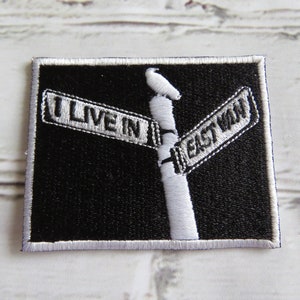 Peut inclure: Patch brodé noir et blanc avec un panneau de rue qui indique "I Live In East Won".