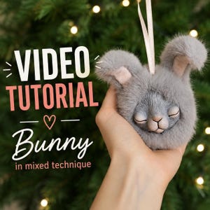 May include: A grey plush bunny ornament with closed eyes and a light pink nose, featuring a soft faux fur texture and a light-colored ribbon loop for hanging. The image includes the text: VIDEO TUTORIAL Bunny in mixed technique.