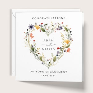 May include: A white engagement card with a floral heart design. The card reads "CONGRATULATIONS" at the top, with the names "ADAM and OLIVIA" in the center, and "ON YOUR ENGAGEMENT" and the date "25.06.2024" at the bottom.