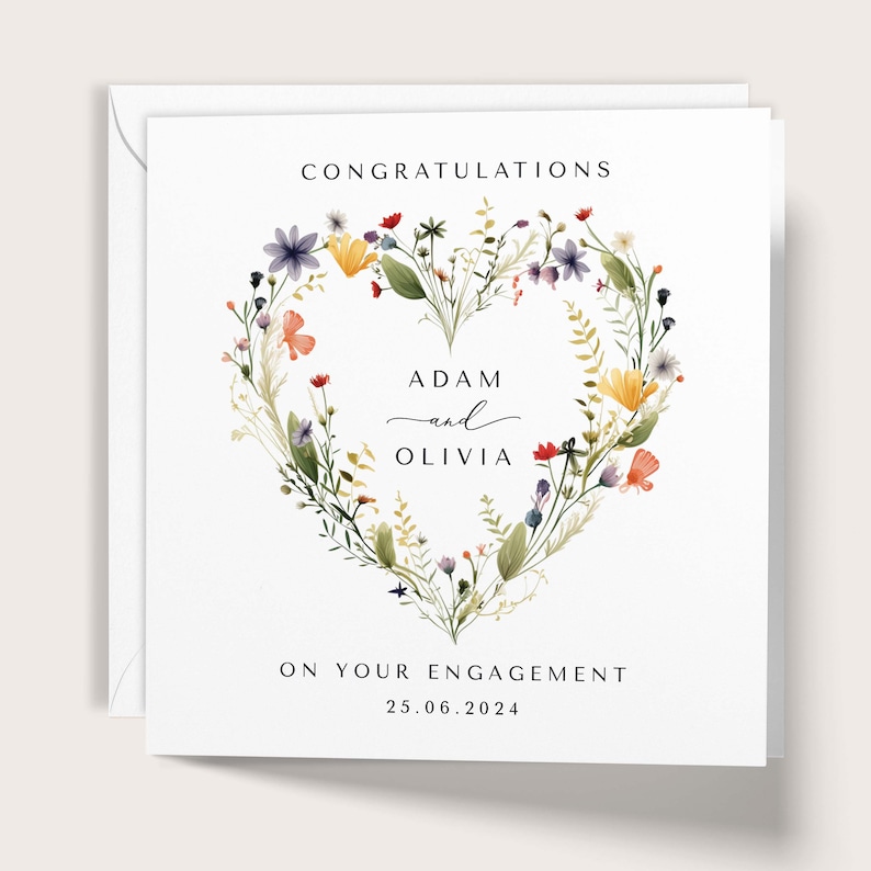 May include: A white engagement card with a floral heart design. The card reads "CONGRATULATIONS" at the top, with the names "ADAM and OLIVIA" in the center, and "ON YOUR ENGAGEMENT" and the date "25.06.2024" at the bottom.