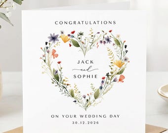 May include: A square white greeting card featuring a heart-shaped wreath of colourful wildflowers. The text reads CONGRATULATIONS, JACK and SOPHIE, ON YOUR WEDDING DAY, and 30.12.2026 in black font centred within the floral heart design.